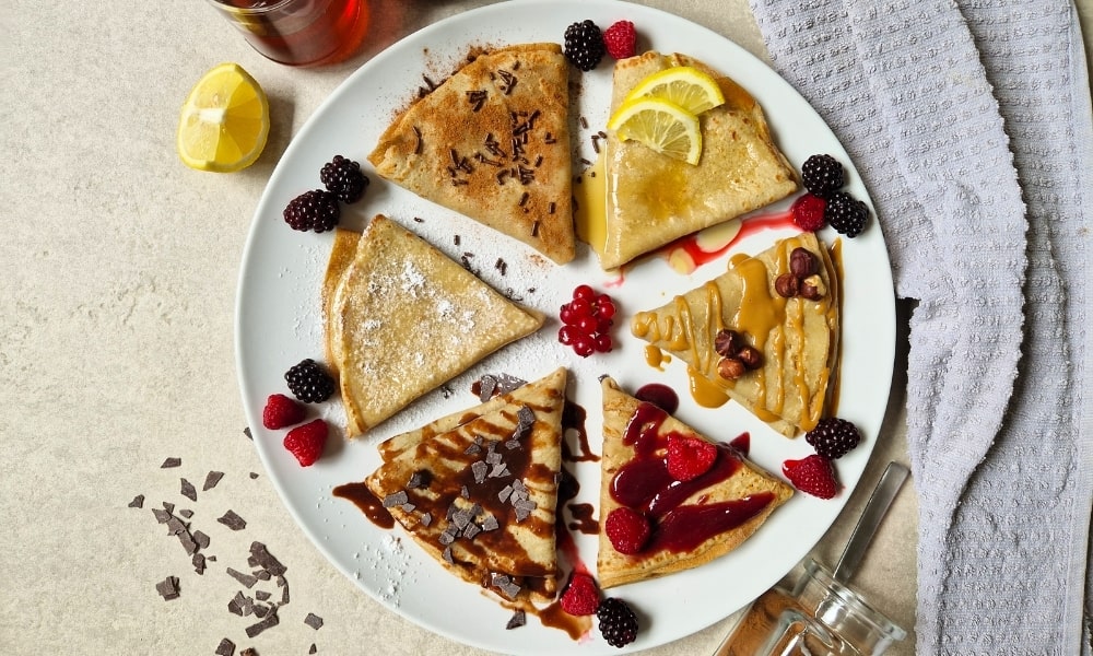 6 Protein Crepes auf einem Teller mit verschiedenen Toppings wie Vetain Haselnussmus und frischen Früchten