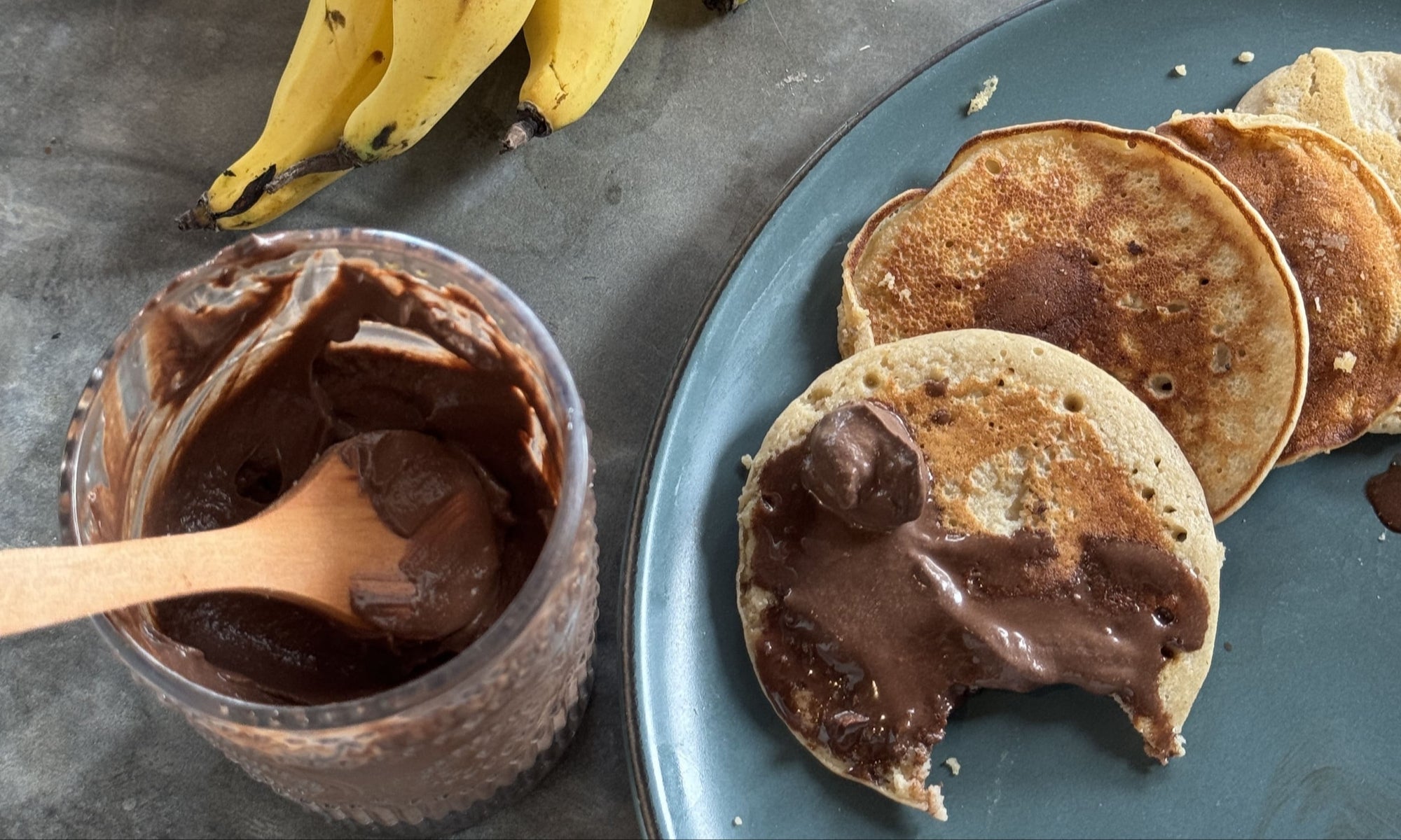Die besten veganen Protein Pfannkuchen: Leckere Pfannkuchen mit Schokocreme auf einem Teller, kleines Glas mit Schokocreme und Bananen daneben