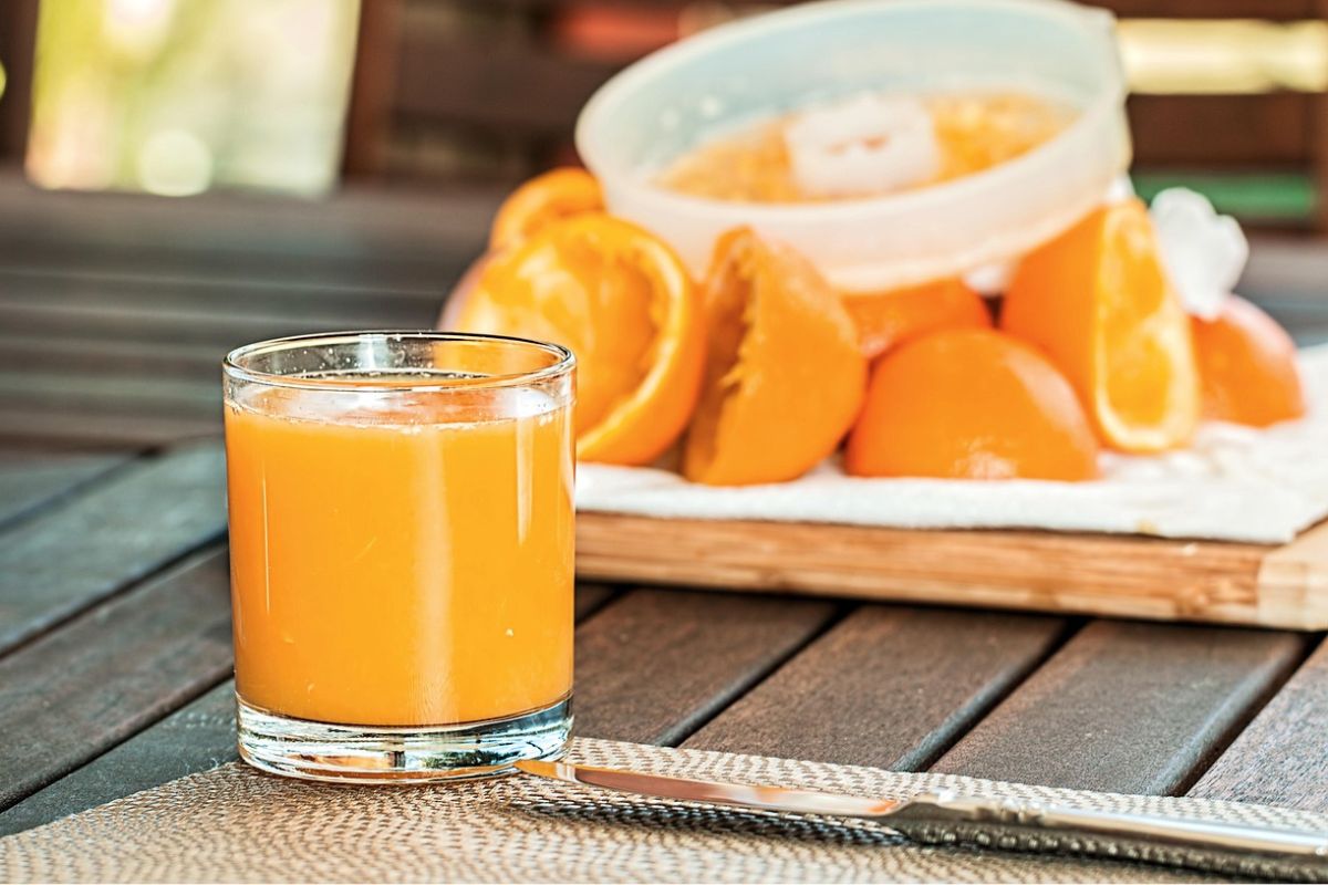 Glas frisch gepresster Orangensaft mit Orangenschalen im Hintergrund