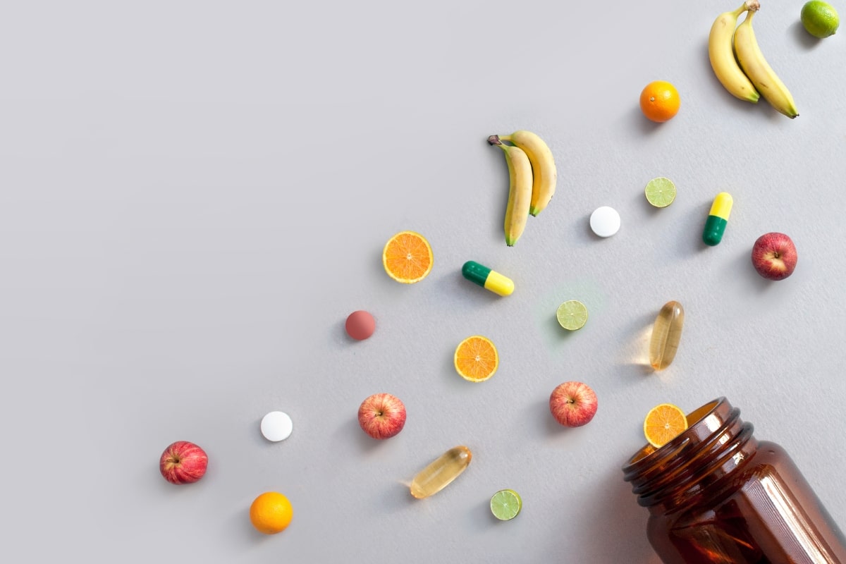 Kapseln, Tabletten und Obst neben einem braunen Supplementglas