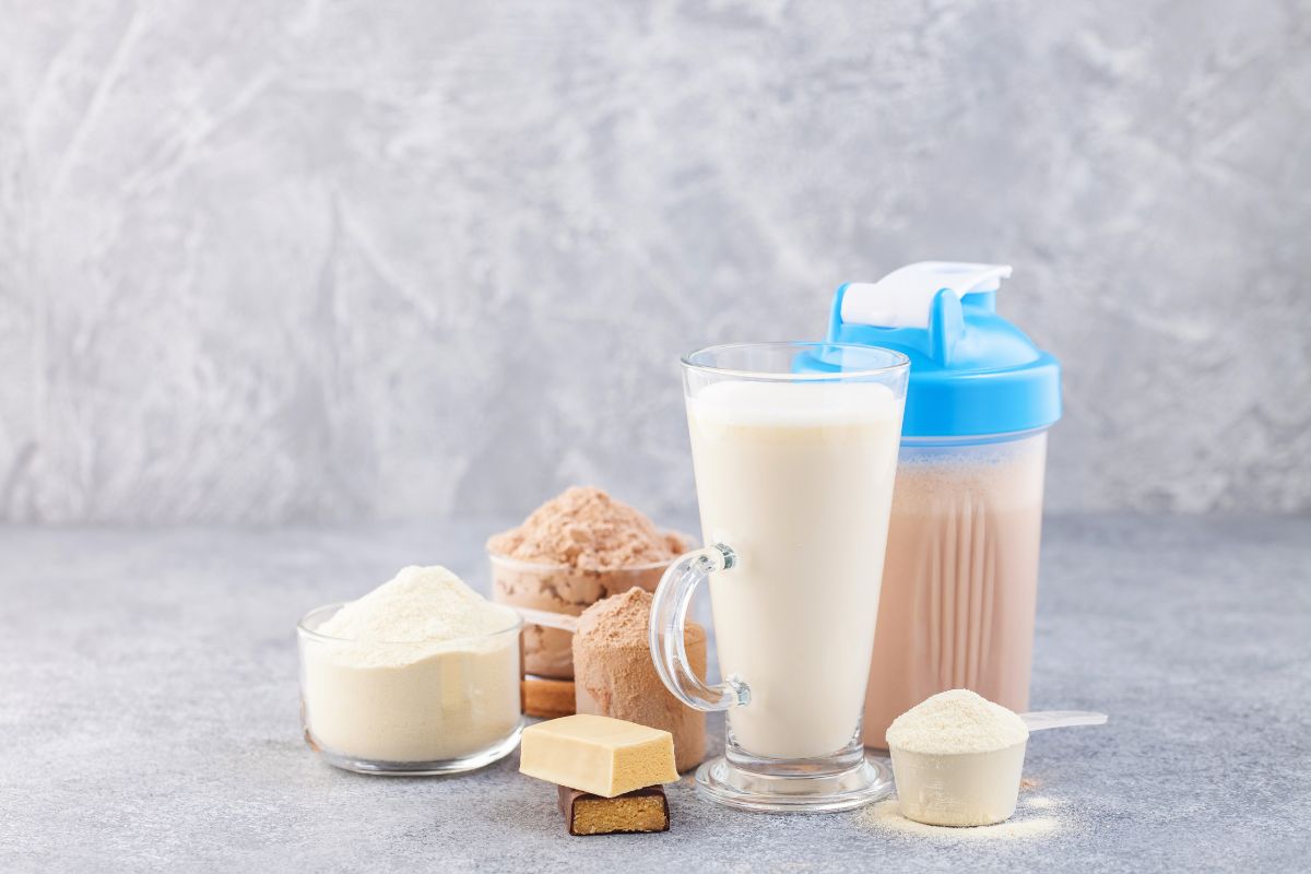 Proteinshakes, Proteinpulver und Proteinriegel in verschiedenen Behältern auf grauem Hintergrund