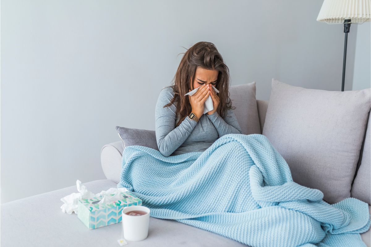 Kranke Frau mit Schnupfen auf dem Sofa mit einer Decke, Tee und Taschentüchern