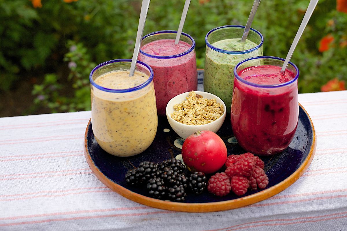 verschiedene bunte, gesunde Smoothies auf einer Platte mit Obst als Beispiel für gesunde, aber leckere Ernährung