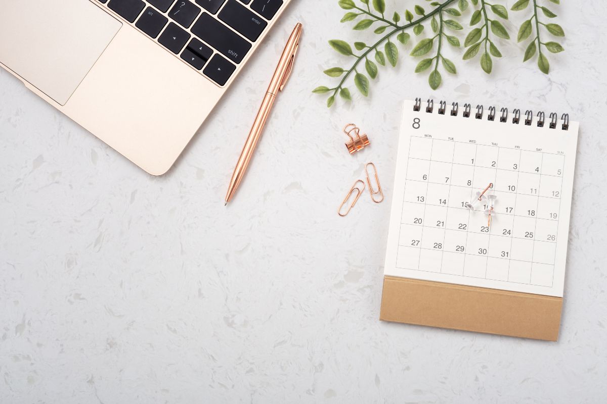 Kalender zum Eintragen von Terminen mit Büroklammern, Laptop und einem Stift