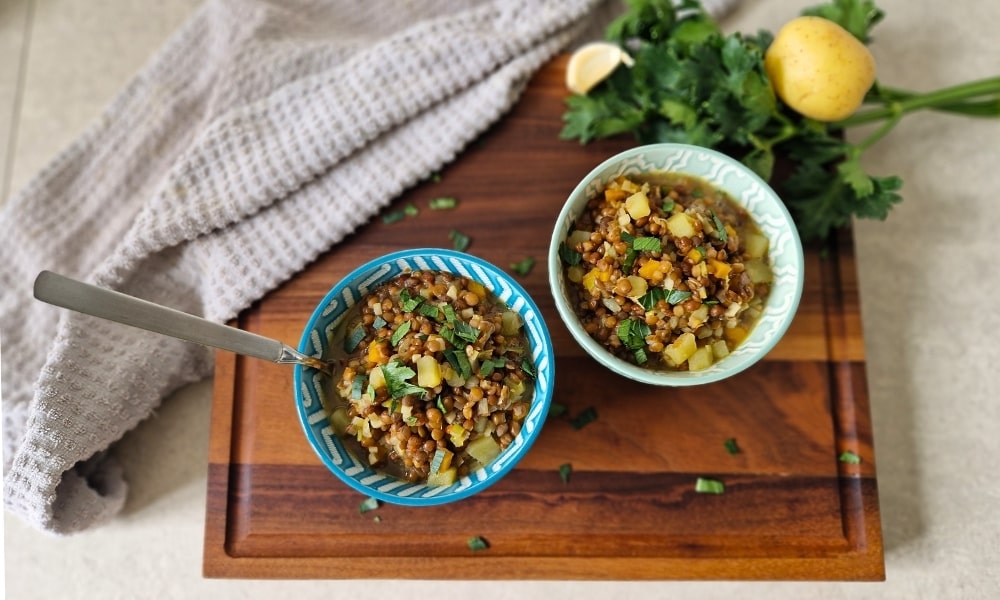 Zwei Schüsseln mit veganem Linseneintopf auf einem Holzbrett, außenrum ein Handtuch und Gemüse als Deko
