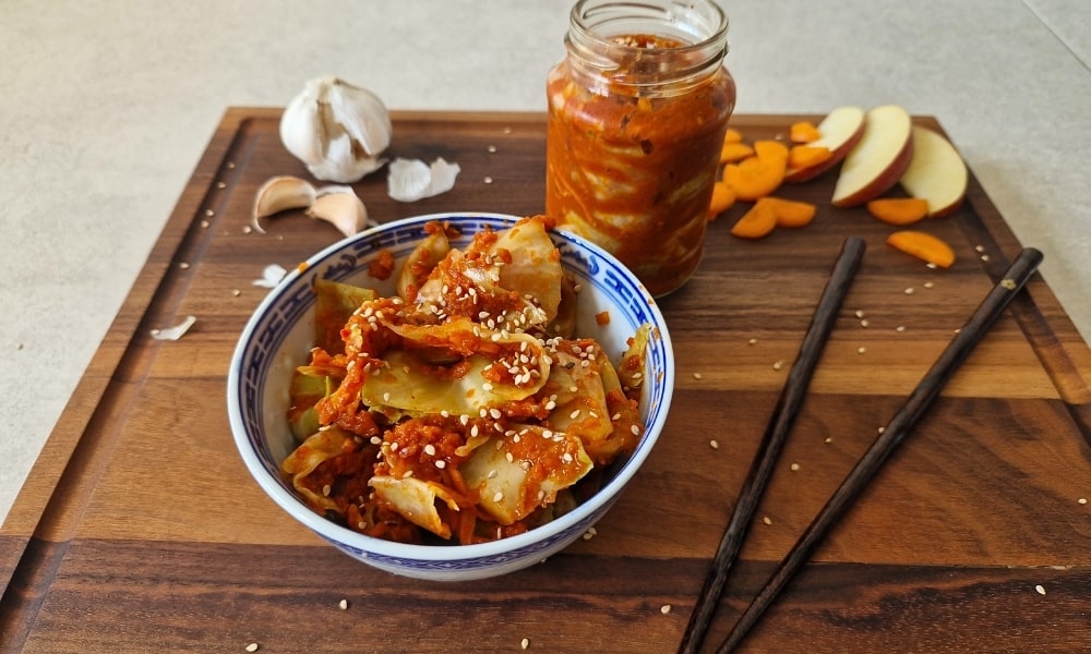 Kimchi vegan in einer Schüssel und im Glas mit Zutaten und Essstäbchen drum herum