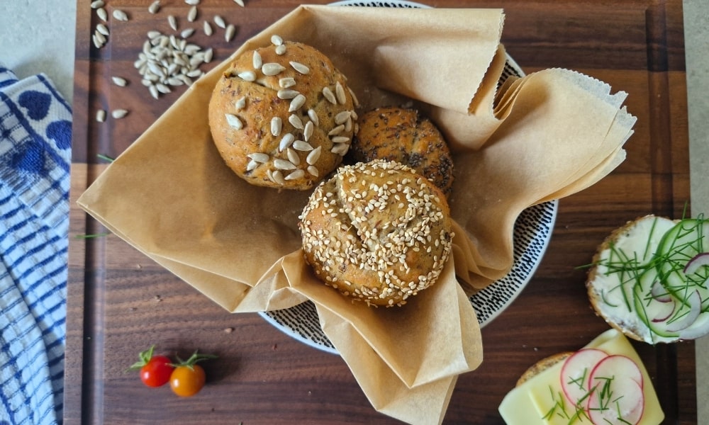Protein Brötchen mit Toppings wie Samen und Kernen in einer Schale, ein Brötchen ist aufgeschnitten und lecker belegt