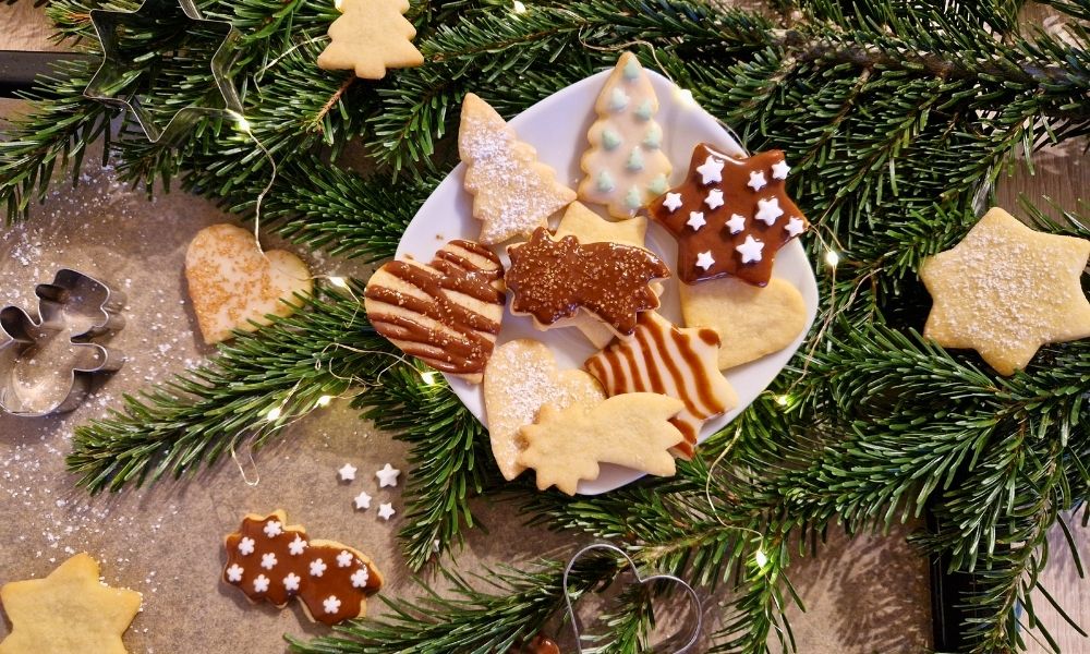 Vegane Plätzchen mit Deko auf einem weihnachtlichen Teller mit Tannenzweig im Hintergrund