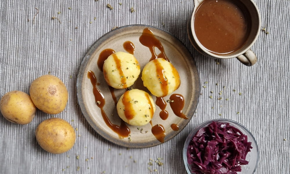 Vegane Kartoffelknödel auf einem Teller, dazu Sauce und Rotkraut