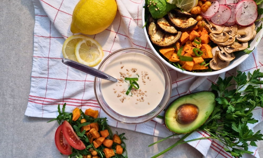 Tahini Sauce, daneben eine Bowl mit frischen Zutaten und Gemüse