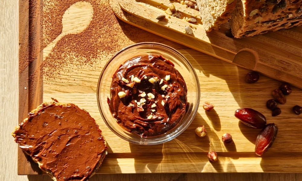Vegane Schokocreme (selbergemacht) in einer Schale. Darunter ein Holzbrett mit Brot