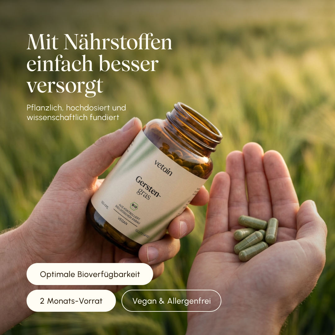 Two hands holding an open bottle of Vetain Barley Grass organic capsules, with several green capsules resting in one palm. Background: blurred barley field in warm sunlight. Text: "Simply better nourished – plant-based, high dosage and scientifically proven." Badges: Ideal bioavailability, 2-month supply, Vegan & allergen-free.