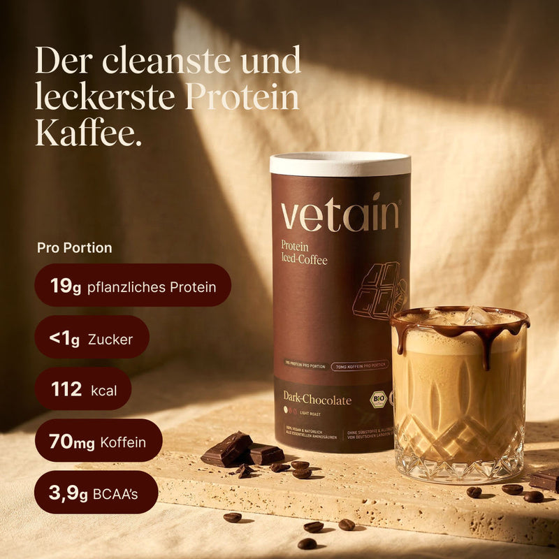 Vetain Vegan Protein Iced Coffee Dose (Dark-Chocolate, Light Roast) und ein Kristallglas mit Iced Coffee und Schokoladendrizzle auf Steinuntergrund, dekoriert mit Kaffeebohnen und Schokoladenstücken. Text: „Der cleanste und leckerste Protein Kaffee." Pro Portion: 19g pflanzliches Protein, <1g Zucker, 112 kcal, 70mg Koffein, 3,9g BCAAs.