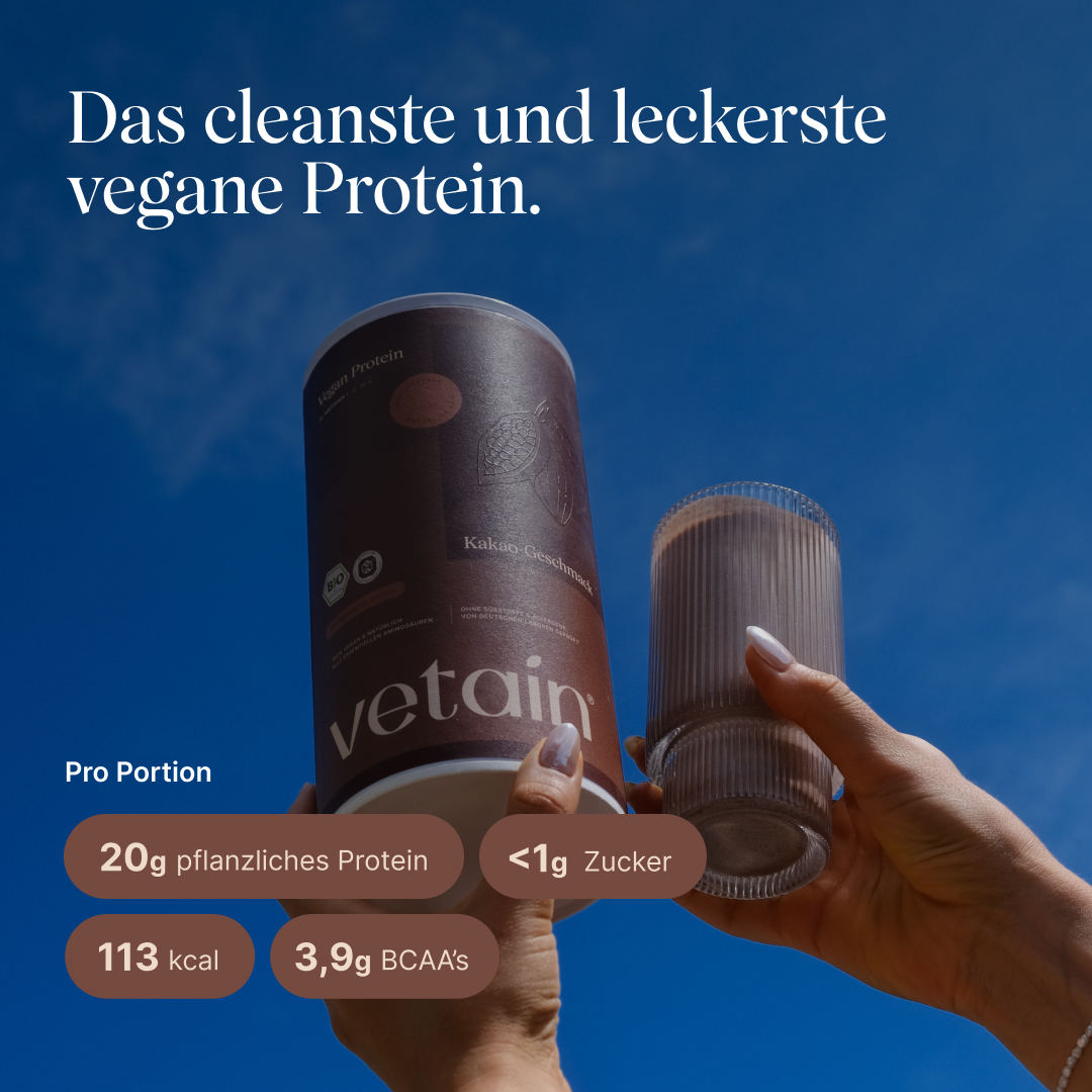 Two hands hold the vetain Vegan Protein tub (cocoa flavor) and a ribbed glass of protein shake against a blue sky. Text: “The cleanest and tastiest vegan protein.” Per serving: 20 g plant-based protein, <1 g sugar, 113 kcal, 3.9 g BCAAs.