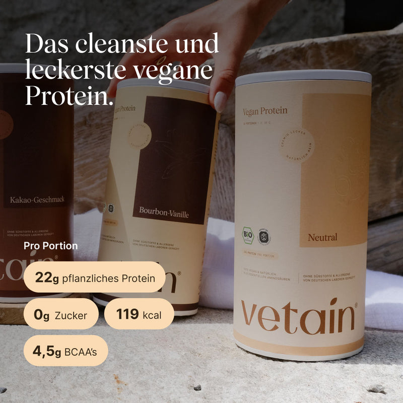Three vetain vegan protein tubs (cocoa flavor, bourbon vanilla, and unflavored) on a stone surface; a hand reaches for the middle tub. The unflavored tub is in the foreground. Text: “The cleanest and tastiest vegan protein.” Per serving: 22 g plant-based protein, 0 g sugar, 119 kcal, 4.5 g BCAAs.