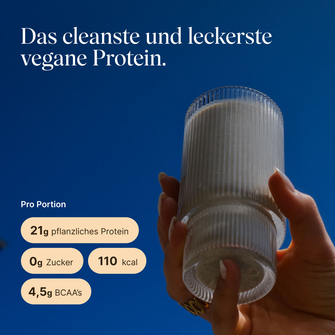 Hand holding a ridged glass of light cinnamon protein shake against a blue sky. Text: “The cleanest and most delicious vegan protein.” Per serving: 21g plant-based protein, 0g sugar, 110 kcal, 4.5g BCAAs.