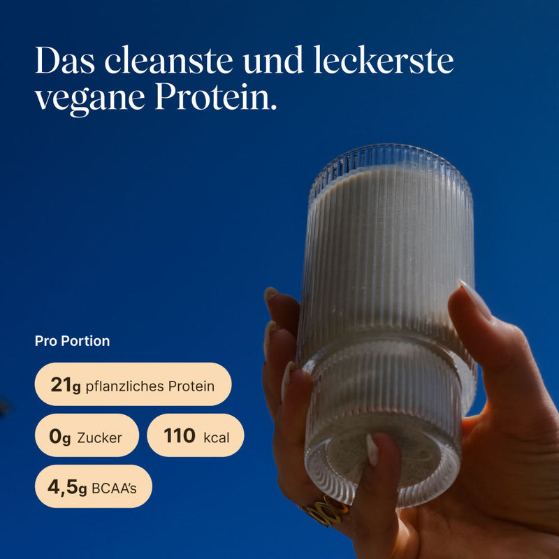 Hand holding a ridged glass of light cinnamon protein shake against a blue sky. Text: “The cleanest and most delicious vegan protein.” Per serving: 21g plant-based protein, 0g sugar, 110 kcal, 4.5g BCAAs.