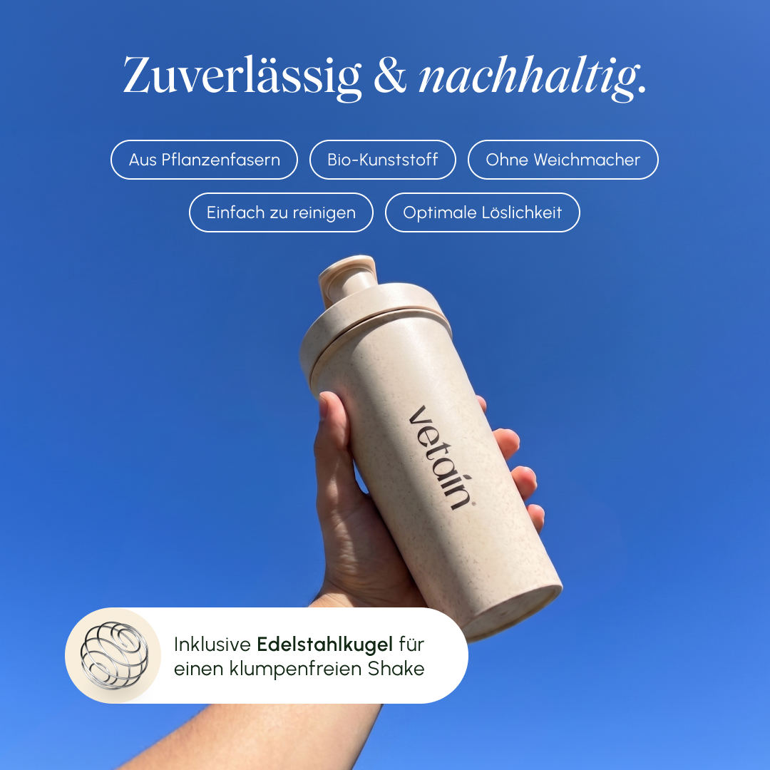 Hand hält vor blauem Himmel einen beigen vetain Shaker; Hinweise: aus Pflanzenfasern, Bio-Kunststoff, ohne Weichmacher, einfach zu reinigen, optimale Löslichkeit, inklusive Edelstahlkugel für einen klumpenfreien Shake.