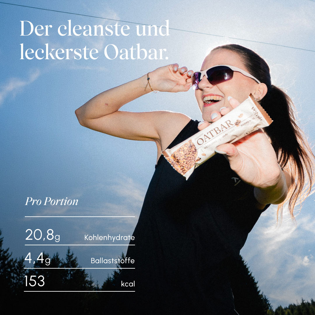 Frau in Sportkleidung hält lachend einen Vetain Oatbar Schoko-Nuss; eingeblendete Nährwerte pro Portion: 20,8 g Kohlenhydrate, 4,4 g Ballaststoffe, 153 kcal. Text „Der cleanste und leckerste Oatbar."