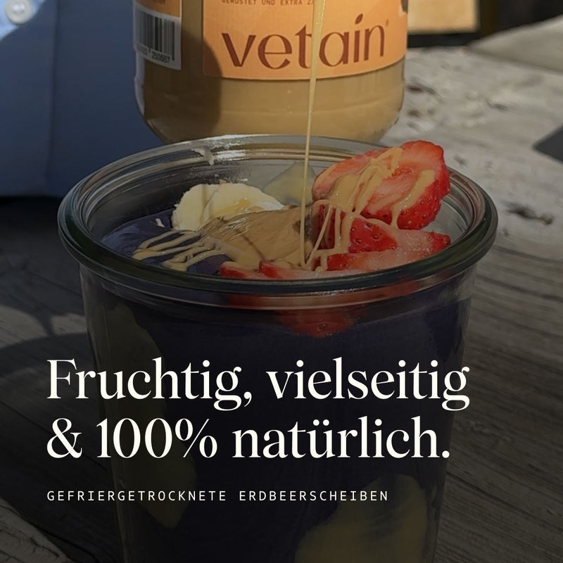 Glas mit Porridge darin und darauf Erdbeerscheiben und Banane und Nussmus. Die Erdbeerscheiben sind fruchtig, vielseitig und 100% natürlich. 