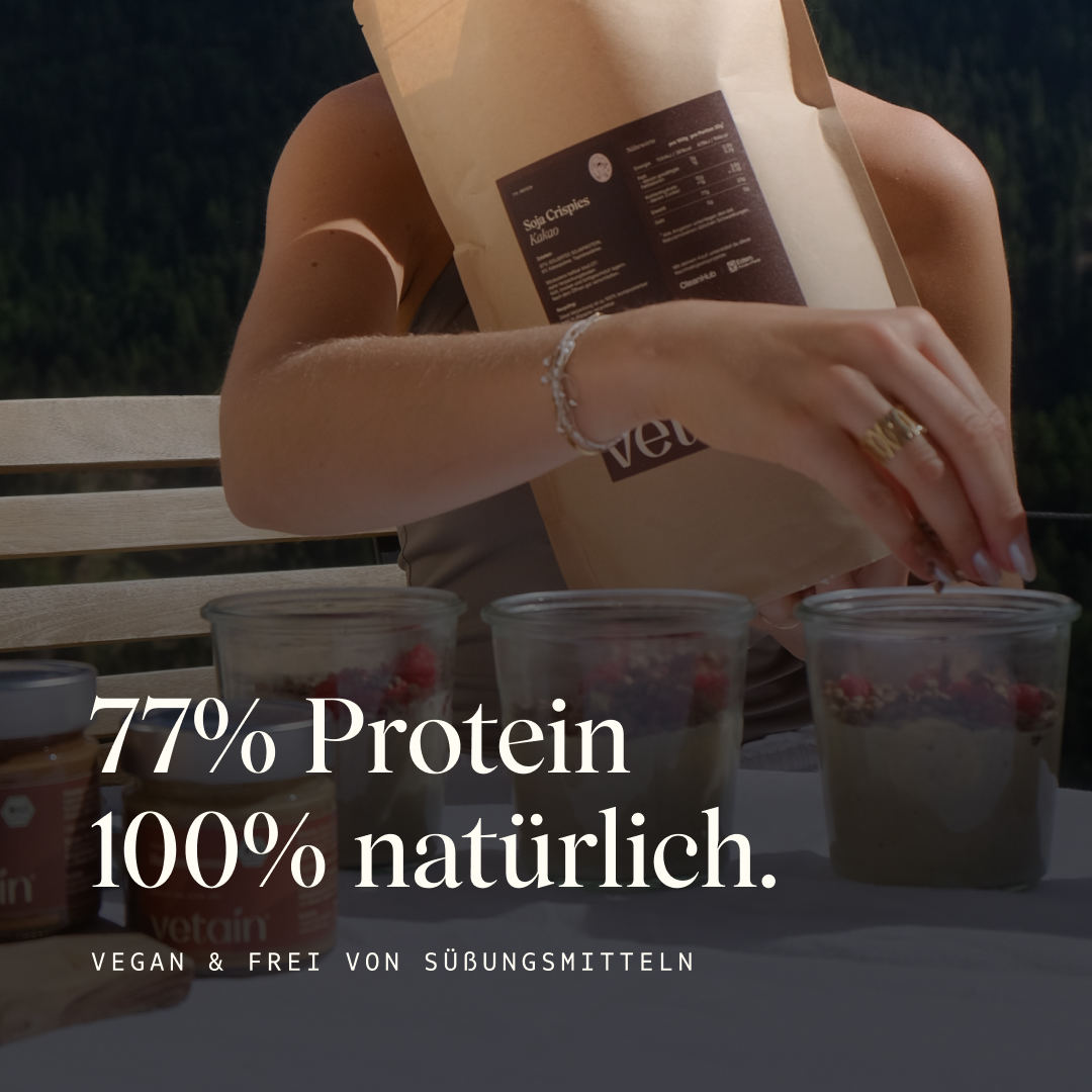 Vetains Soja Crispies mit 77% Protein, 100% natürlich. Vegan und frei von Süßungsmittel. Auf dem Bild greift eine Frau in die Soja Crispies Verpackung, davor stehen drei Gläser mit Reispudding und Himbeeren als Topping