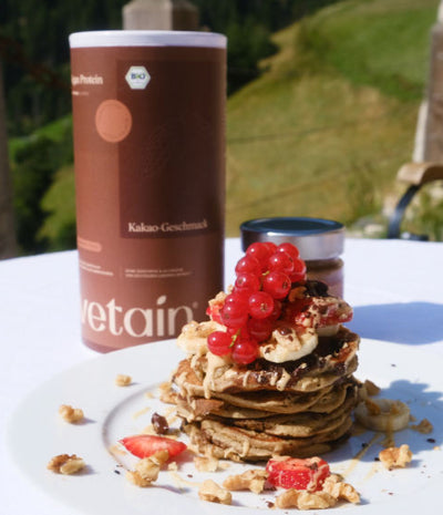 Vegane Pancakes mit Beeren darauf und im Hintergrund eine Dose Vetain vegan Protein Kakao